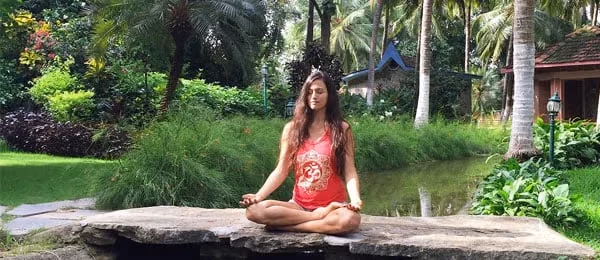 A woman seated in meditation beside a pond.