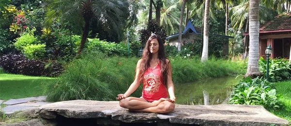 Una donna seduta in meditazione accanto a uno stagno.