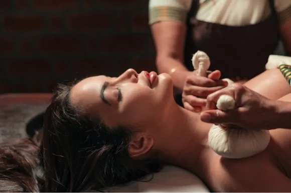 Therapeut van Kairali drukt tijdens de therapie een warm kruidenkompres tegen de nek van een achteroverliggende patiënt