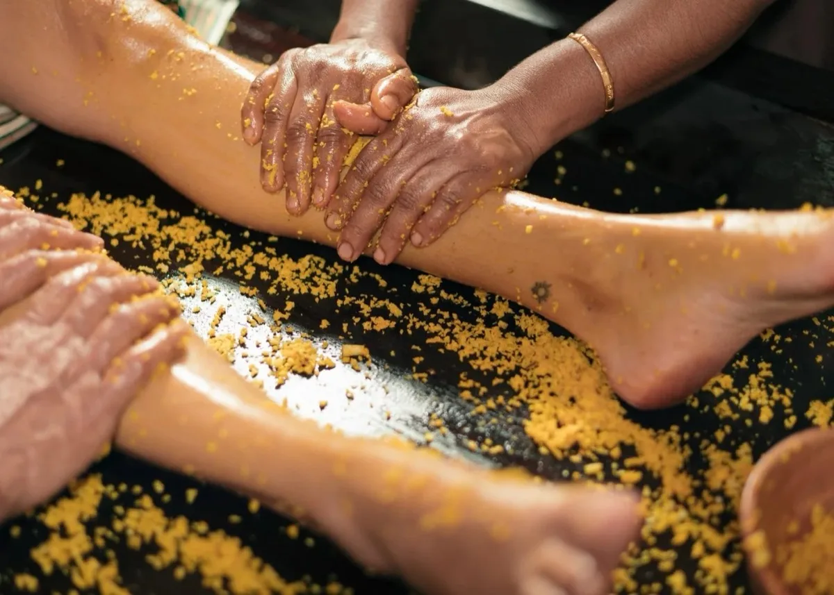 Therapeuten masseren de benen van een persoon tijdens een ayurvedische behandeling.
