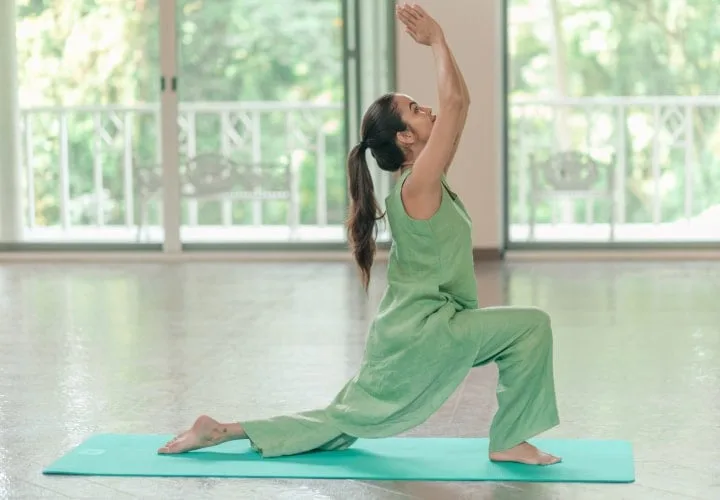 Patiënt oefent een ondersteunde yogalunge op een mat in een lichte studio bij Kairali