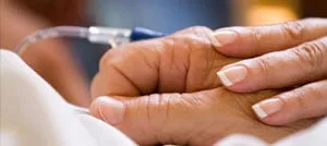 Una mano appoggiata sulla mano di un paziente collegata a una flebo endovenosa