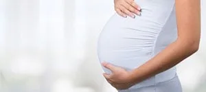Donna incinta con una maglia bianca che appoggia entrambe le mani sull'addome