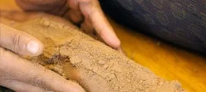 Primo piano di mani che strofinano una polvere di erbe marrone e grossolana lungo l'arto di un paziente