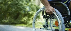 La mano di un uomo sulla ruota di una sedia a rotelle lungo un sentiero alberato all'aperto