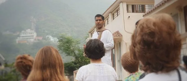 Ein Mann in weißer Kurta und Schal spricht im Freien an einem Hang zu einer Gruppe von Frauen