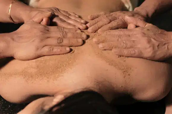 치료사 두 명의 네 손이 환자의 맨 등에 허브 가루를 문지르는 모습