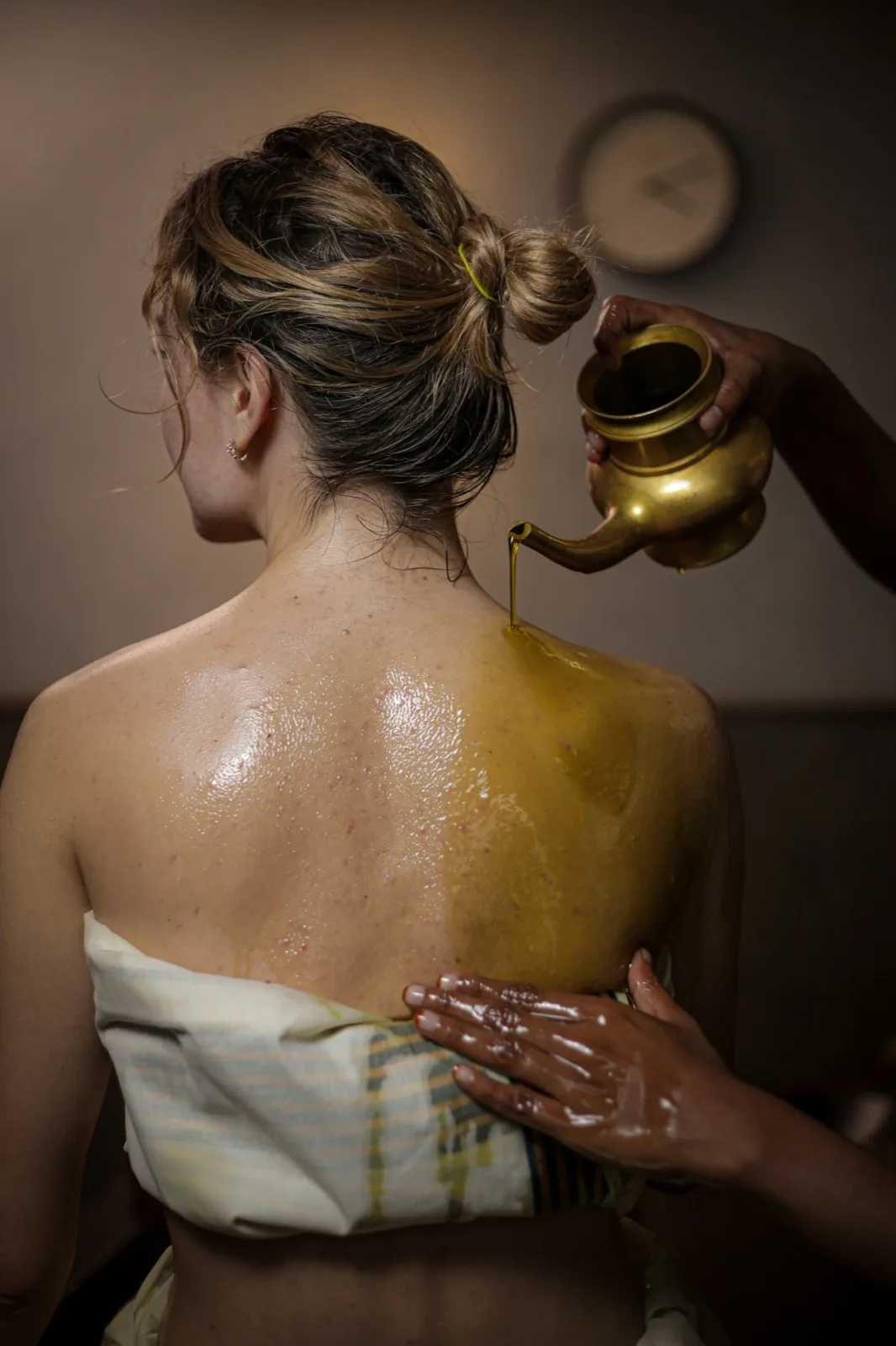 Pizhichil: close view from behind of warm herbal oil being poured from a brass vessel onto a patient's back