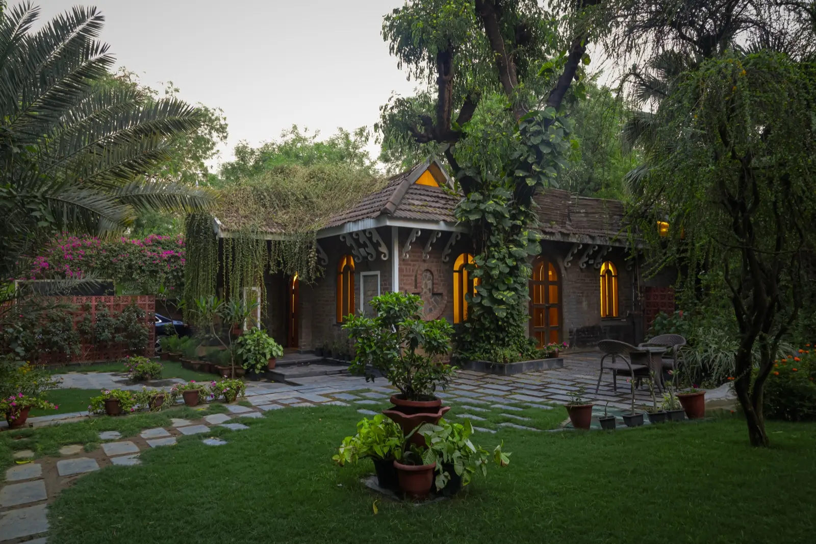 黄昏时分的砖砌小屋风格 Kairali 中心建筑，拱窗透出暖光；瓦顶覆满藤蔓
