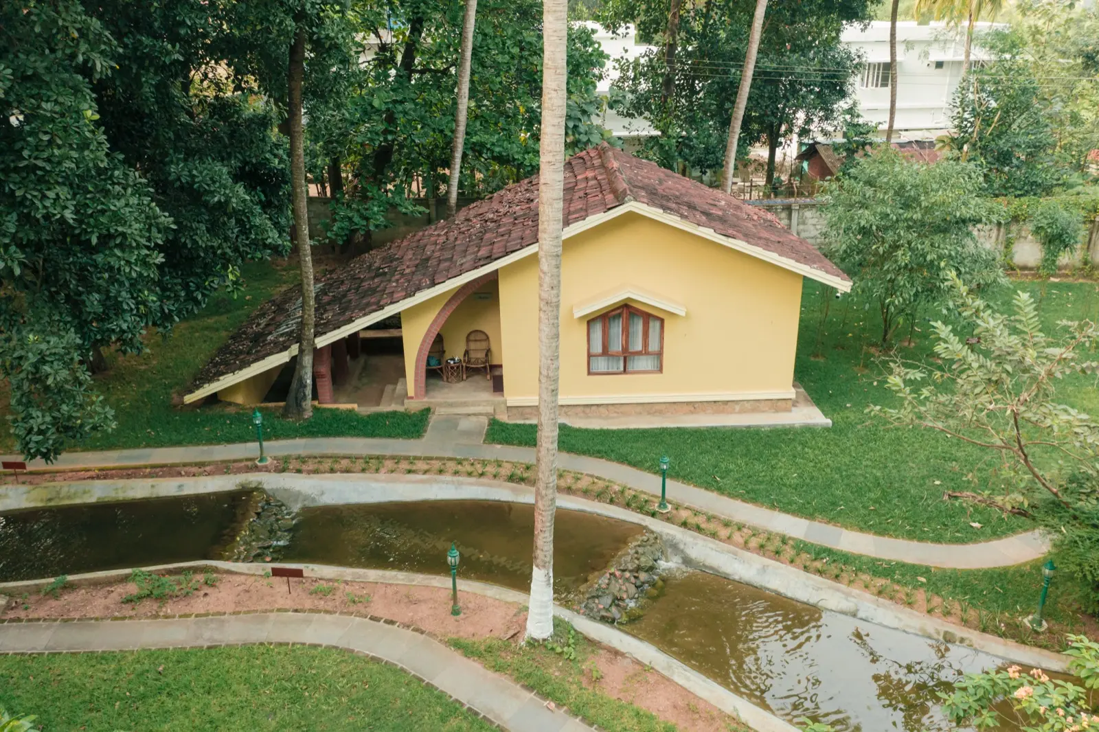 俯瞰一座黄色患者小屋，舒展的瓦顶下是拱形门廊，门廊里放着藤椅