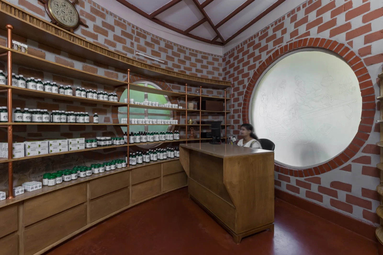 Dispensario della farmacia ayurvedica interna con scaffali curvi in legno di medicinali classici; un membro del personale al banco