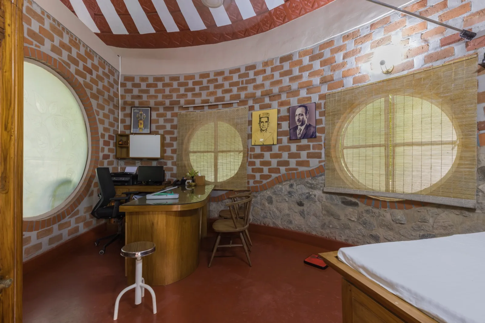 Studio medico per le consulenze con scrivania curva in legno; computer; sgabelli e sedie; finestre rotonde in vetro satinato con tende di bambù