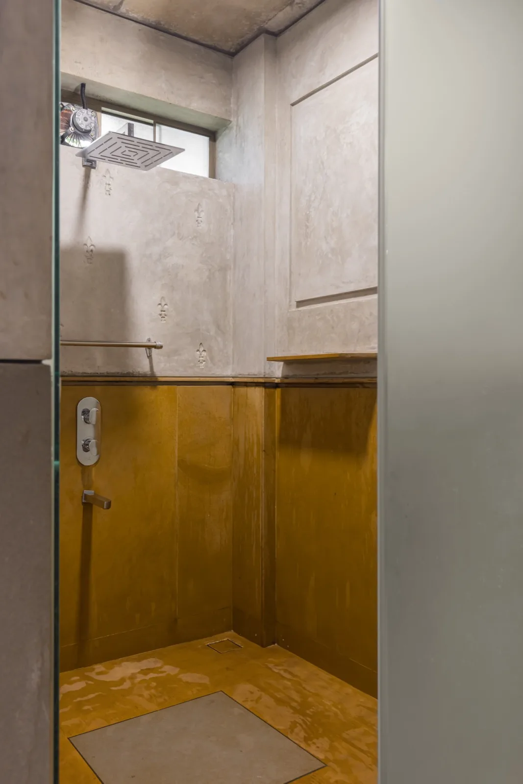 Box doccia con soffione a pioggia; zoccolatura in ossido giallo e pareti in intonaco di calce con motivi floreali; visto attraverso una porta bordata di specchi