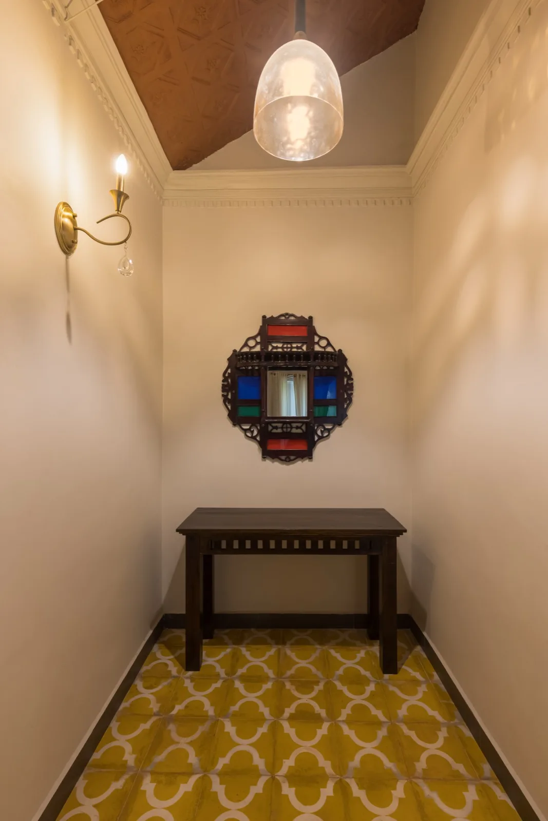Vestibolo d'ingresso di una suite con consolle in legno scuro; pannello intagliato a parete con vetri colorati e un piccolo specchio