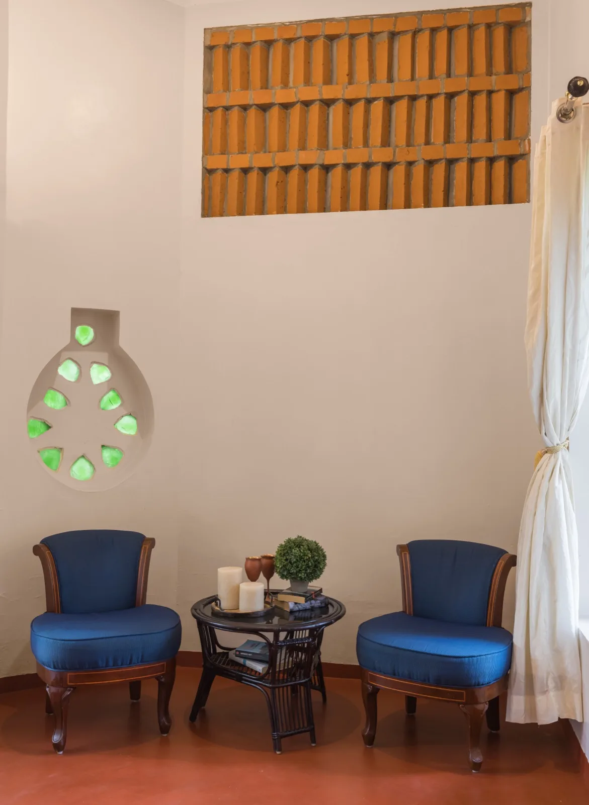 Angolo salotto all'interno di una villa per pazienti con due poltrone imbottite blu; tavolino in rattan con candele e libri