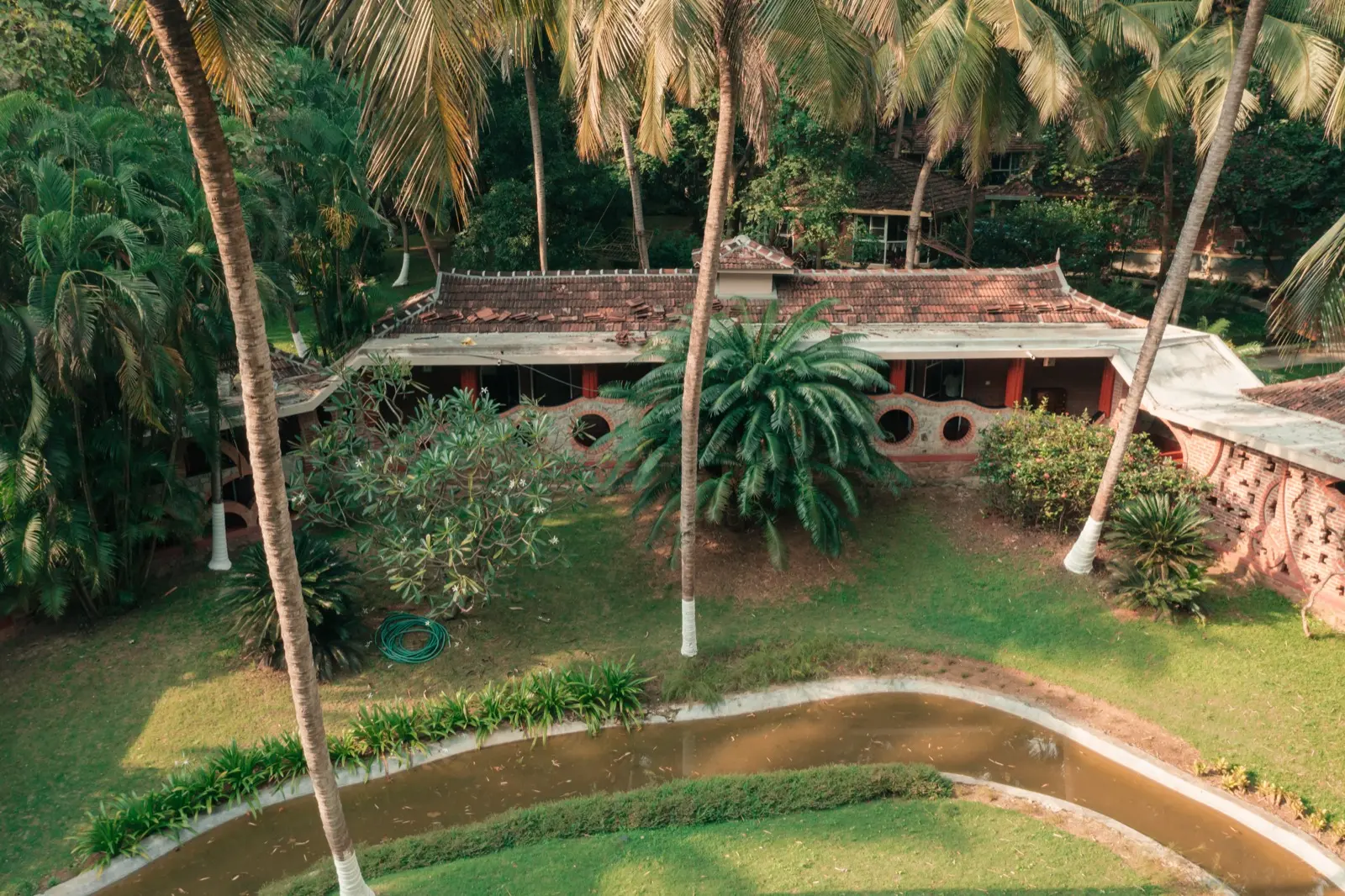 Veduta dall'alto di un lungo edificio con tetto di tegole, facciata in mattoni di laterite e finestre circolari tra le palme