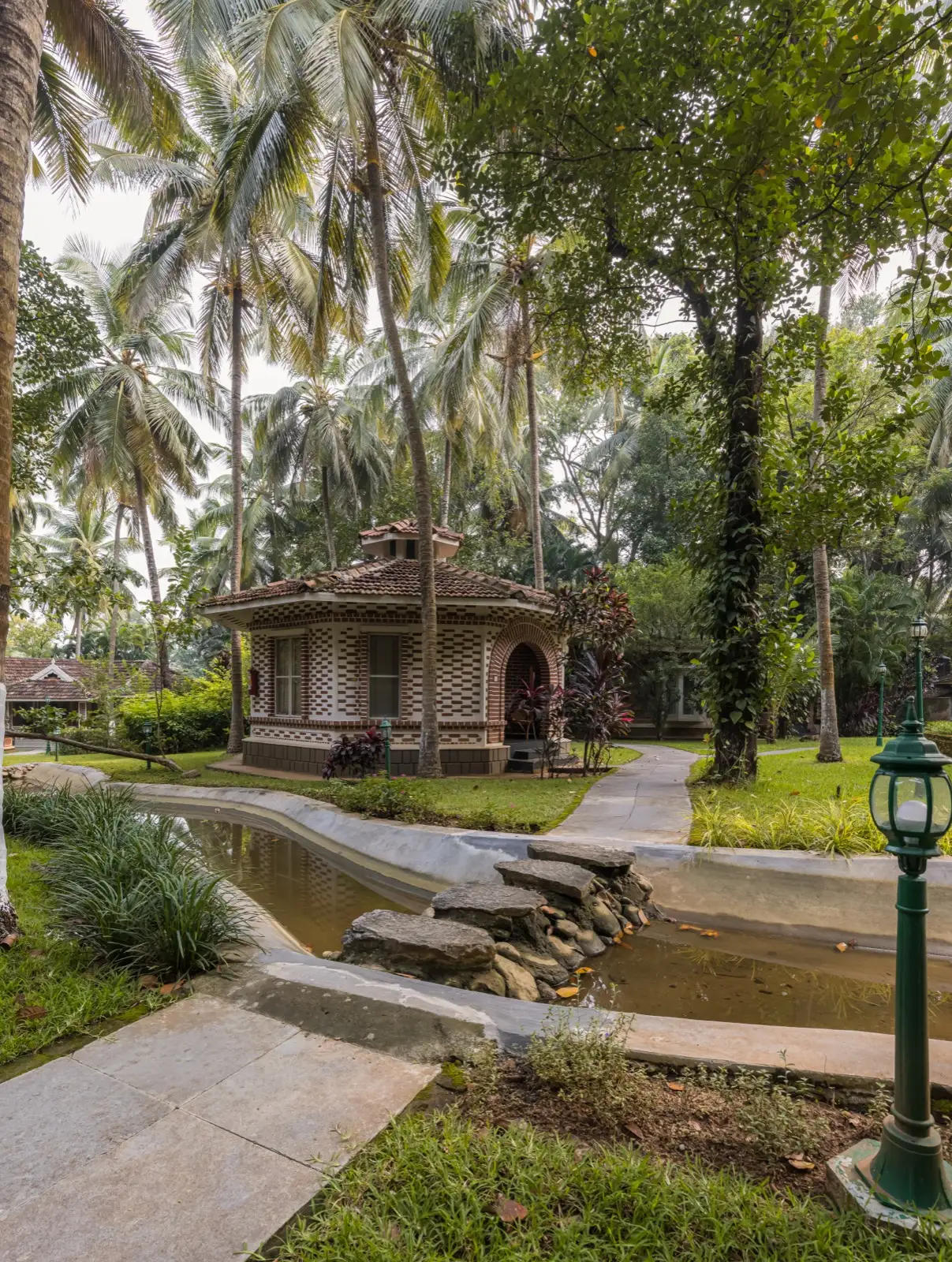 Cottage ottagonale in mattoni tra le palme da cocco, con un canale d'acqua paesaggistico e pietre di passaggio in primo piano