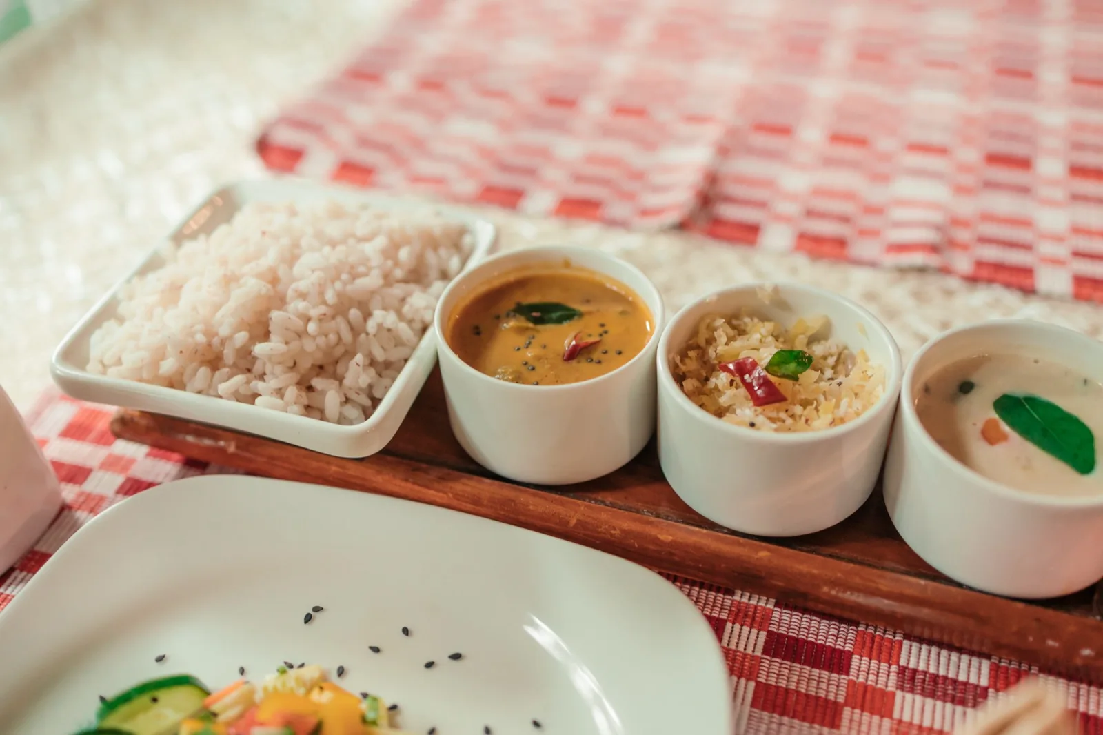 وجبة غذائية أيورفيدية على صينية خشبية: أرز أحمر (ماتا) في طبق مربع مع ثلاثة أوعية صغيرة من الكاري