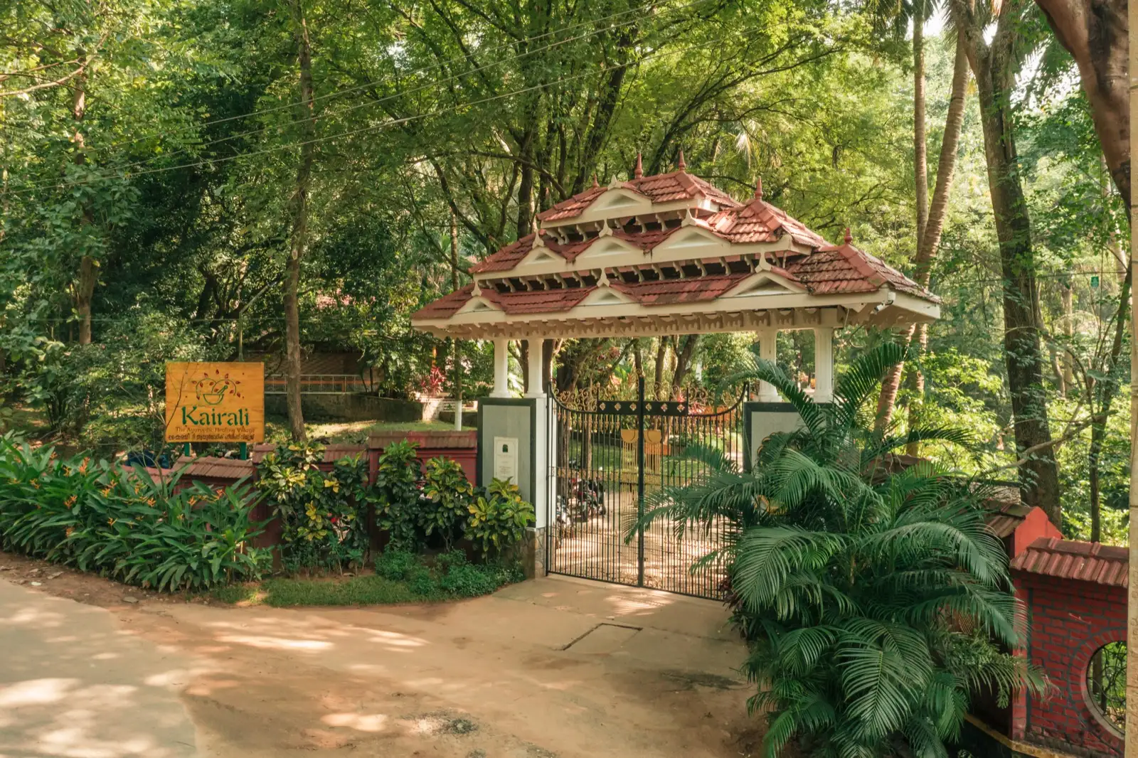 왼쪽에 Kairali The Ayurvedic Healing Village 목재 간판이 있는 정문
