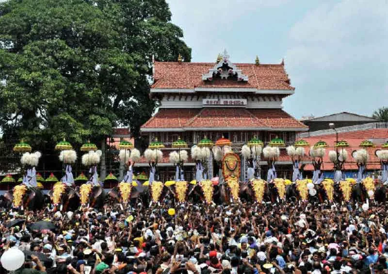 Eine Reihe geschmückter Elefanten vor einem Kerala-Tempel mit Ziegeldach, beobachtet von einer dichten Menschenmenge