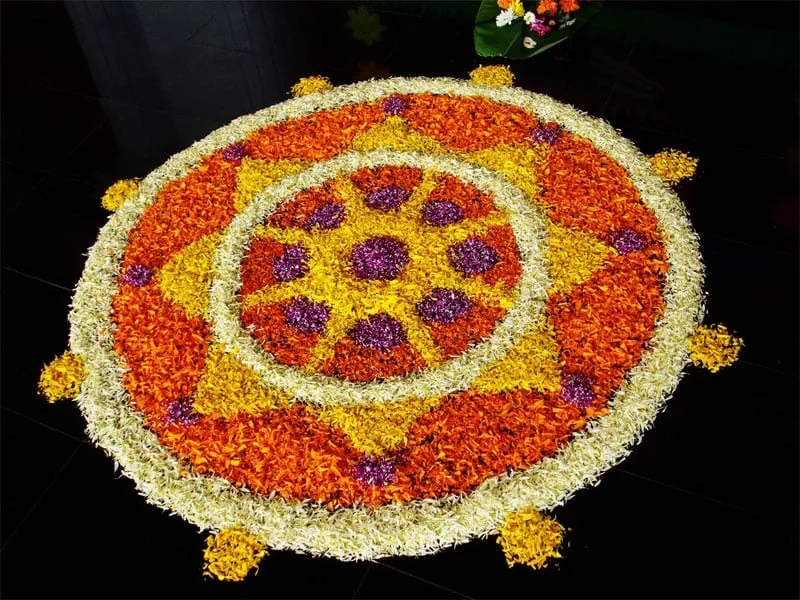 Kreisförmiger Blumenteppich aus Ringelblumen sowie weißen und violetten Blütenblättern auf dunklem Boden