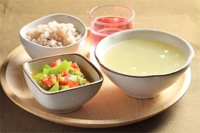 صينية خشبية تحمل عصيدة أرز وأرزًا أحمر وطبقًا جانبيًا من الخضار ومشروبًا ورديًا