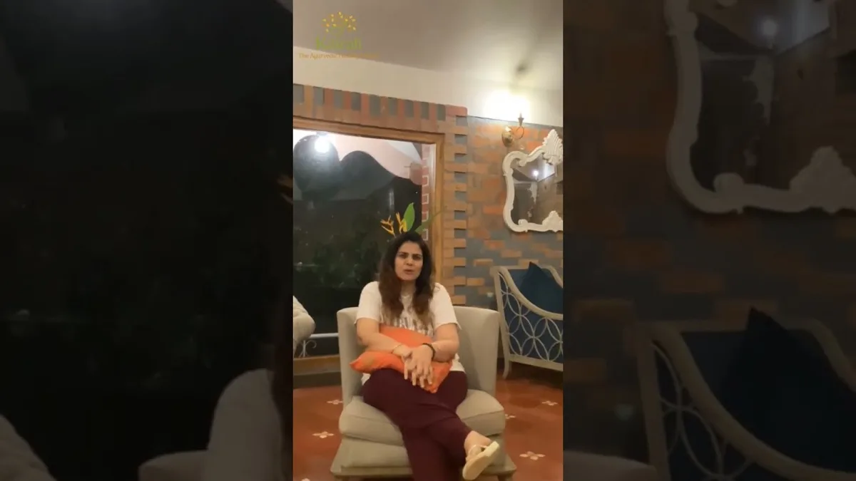 Vrouw in een fauteuil met een oranje kussen, die spreekt in een zitkamer met bakstenen muren